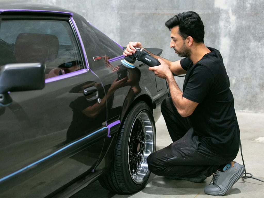 A man is working on a black car, illustrating the steps involved in the car paint enhancement process.