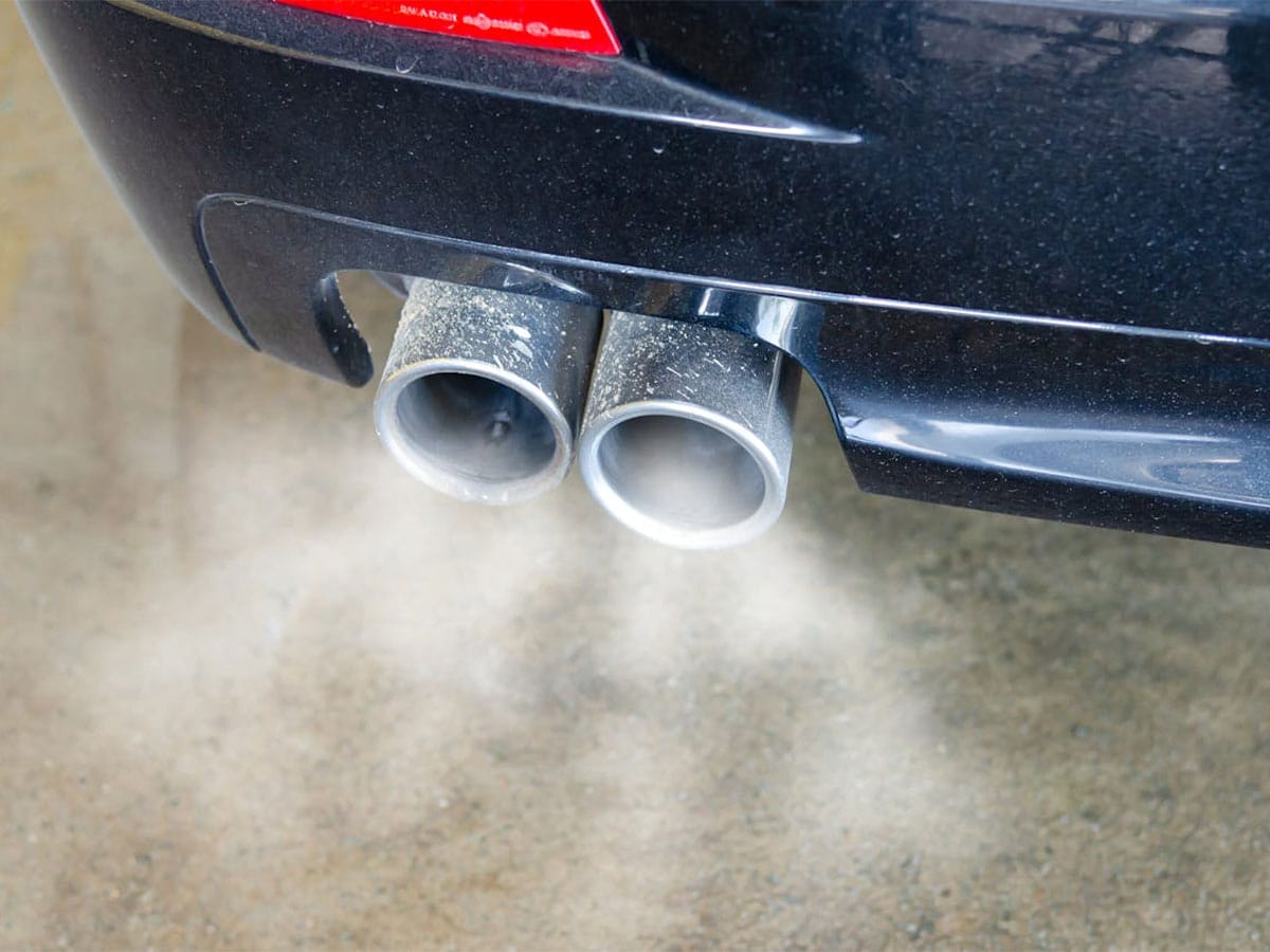 A car exhaust pipe emits smoke, indicating potential issues like a gas smell from the exhaust.